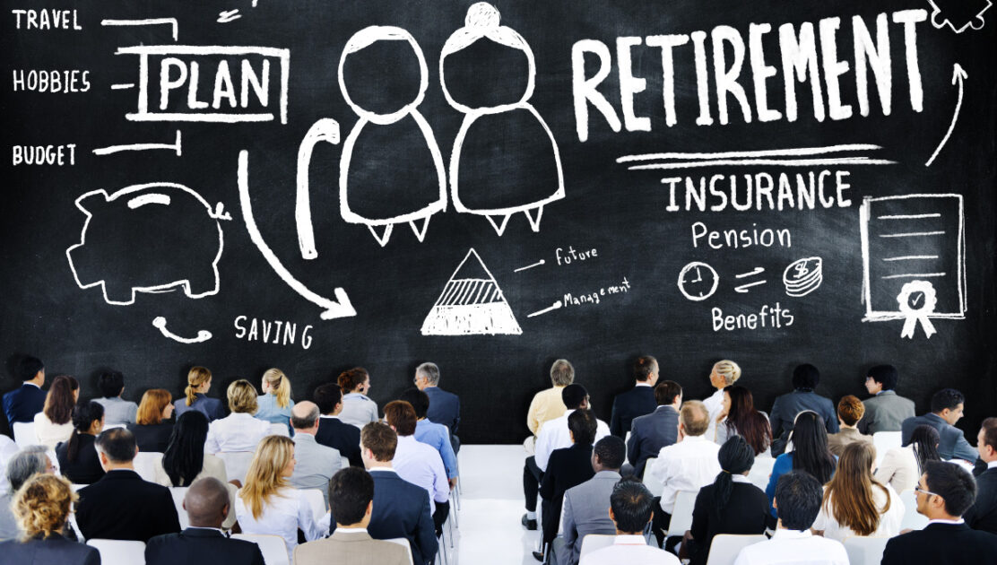A group of employees at a business are sitting in front of a blackboard with retirement plan information.