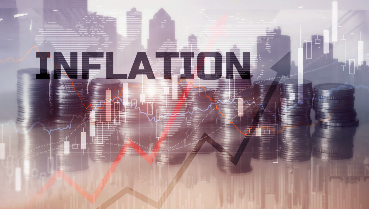 The word inflation over a backdrop of coins and a cityscape with graph arrows pointing up indicating rising rates.